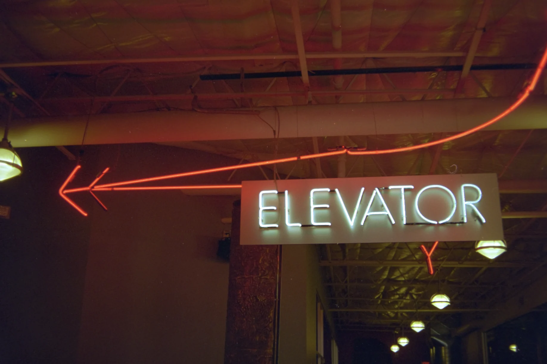 The same frame converted: a red neon arrow and a white neon ELEVATOR sign in a dim industrial corridor.